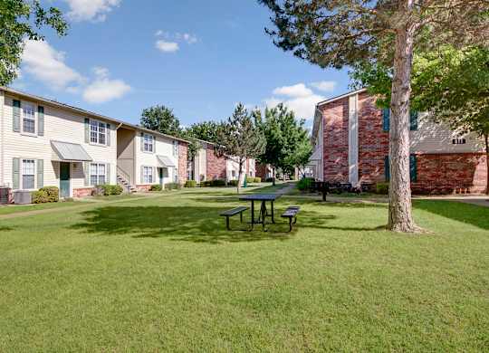 A grassy area with a picnic table and benches in front of apartment buildings.