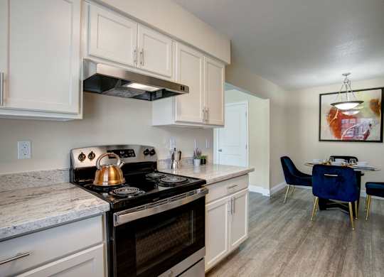 A bright kitchen here at Indigo with white cabinetry, light countertops, and black appliances including an oven and range hood. A nearby dining area with modern lighting and comfortable seating creates a clean, inviting space for everyday living.