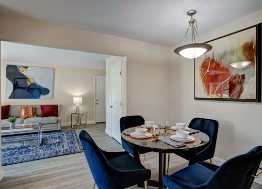 A dining room with a table set for four and a painting on the wall.