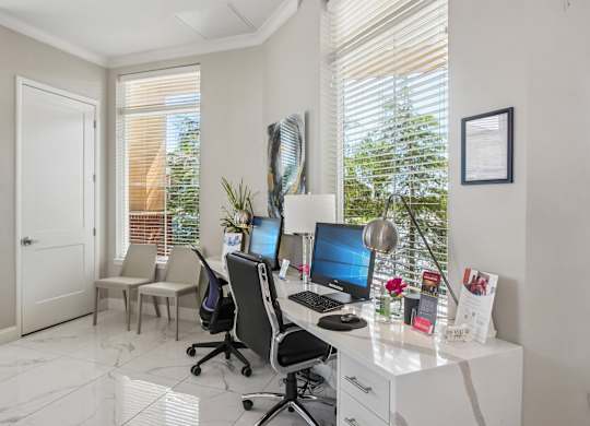 A white desk with a computer and a chair in front of a window with blinds.