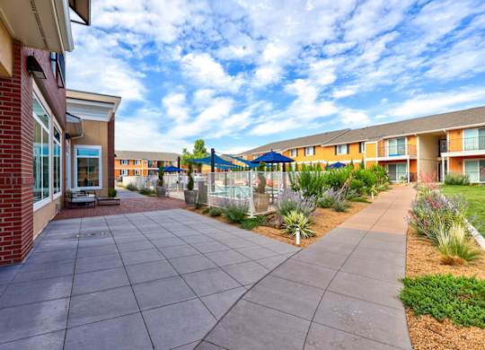 A long concrete walkway leads to a building with a brick wall on the left.