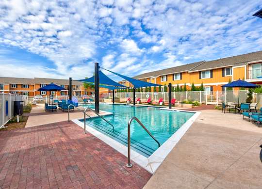 A pool surrounded by a brick patio and umbrellas.