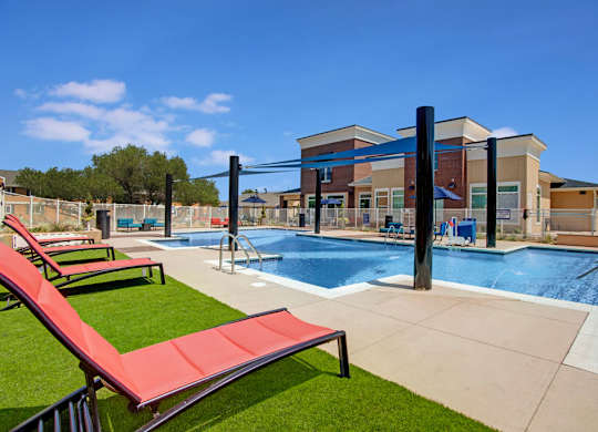 A pool with red sun loungers and a building in the background.