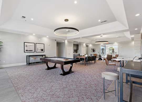 A spacious resident lounge here at Lincoln at Central Park with plush carpet flooring, a pool table, dining table seating, and modern circular ceiling lighting. A neutral color palette and comfortable seating areas create a welcoming, upscale gathering space.