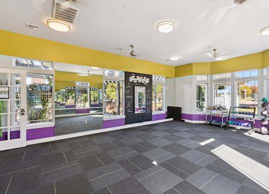 A bright fitness studio here at Lincoln at Central Park with mirrored walls, large windows, and colorful accent walls. A rack of dumbbells and exercise equipment sits nearby, creating an energetic, open space for group workouts or stretching.