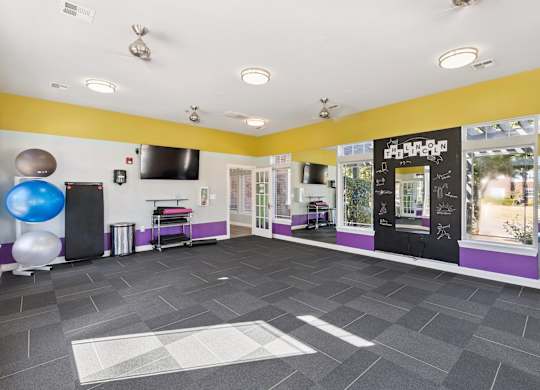 A spacious fitness studio here at Lincoln at Central Park with large windows, mirrored walls, and bright accent colors. A mounted TV, exercise balls, and workout mats create a versatile, motivating space for fitness classes or personal workouts.