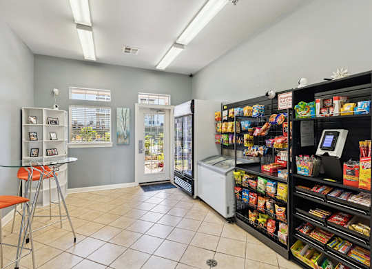 A convenient snack and refreshment area here at Lincoln at Central Park with stocked shelves of snacks, drinks, and grab-and-go items. A glass door and windows bring in natural light, creating a bright, easy-access resident amenity space.