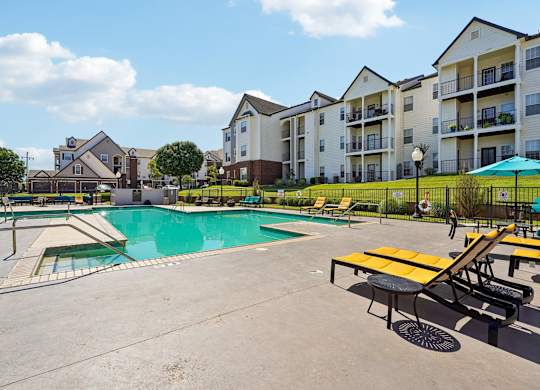 A swimming pool surrounded by a concrete patio and a yellow picnic table.