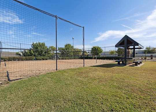 A black fence surrounds a green field with a pavilion in the background.