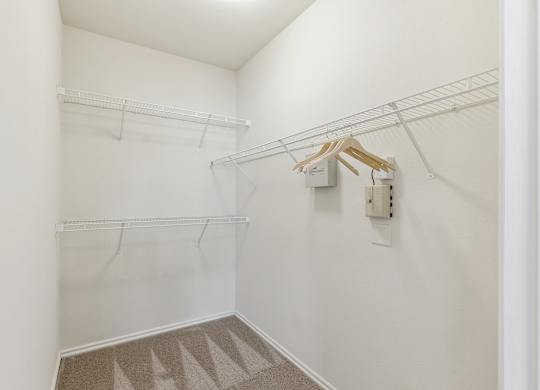 A walk-in closet here at Quail Landing with white wire shelving on two walls, neutral carpet flooring, bright white walls, and a clean, empty layout offering simple storage space.