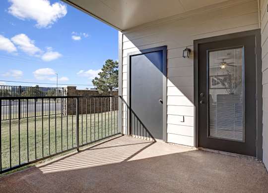 A private patio here at Stoneleigh on May with a covered concrete floor, metal railing, and exterior storage closet. An outdoor door with blinds connects to the living space, offering a bright, open, and relaxing outdoor retreat.