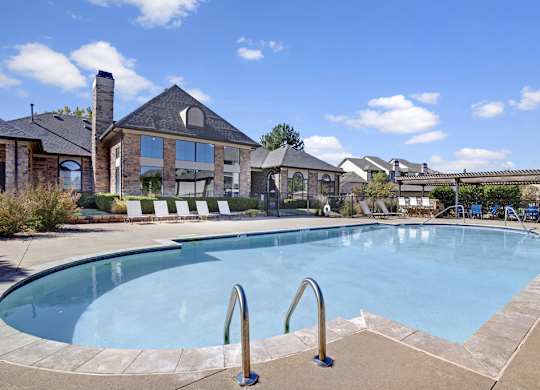 A resort-style swimming pool here at Stoneleigh on May with clear blue water, poolside lounge chairs, and surrounding greenery. A clubhouse backdrop and open sky create a relaxing, community-focused outdoor setting.