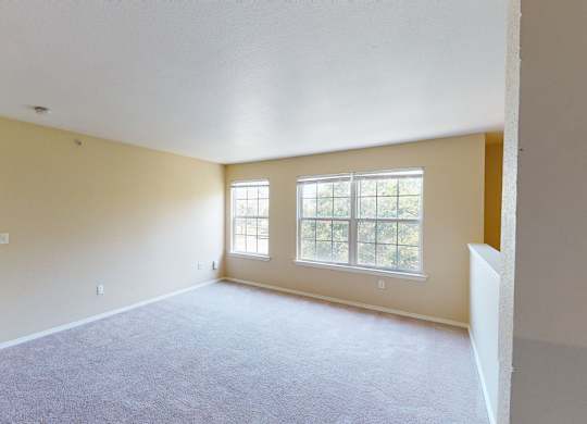A spacious room with a carpeted floor and two windows.