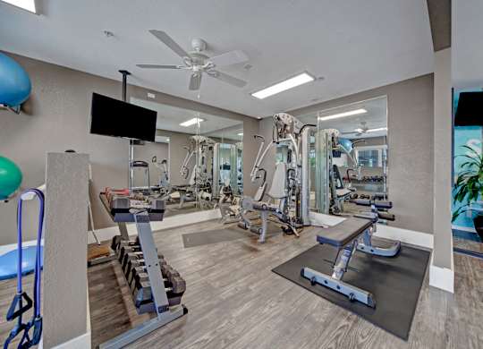 A spacious gym with a variety of equipment and a television mounted on the wall.