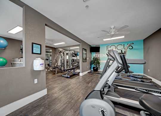 A gym with treadmills, exercise balls, and a ceiling fan.