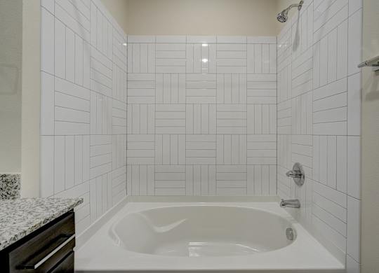 A white tiled bathroom with a white bathtub and a marble countertop.
