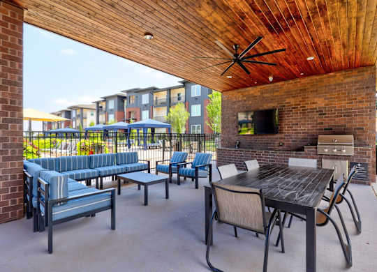 A patio with a brick fireplace and blue chairs.
