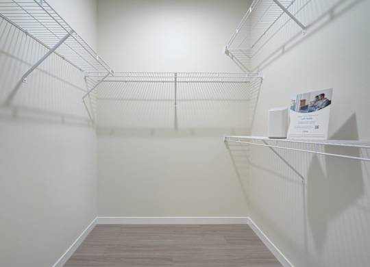 A walk-in closet here at The Encore with white wire shelving on three walls, soft neutral walls, and wood-style flooring. The empty space feels bright, clean, and practical for organized storage.