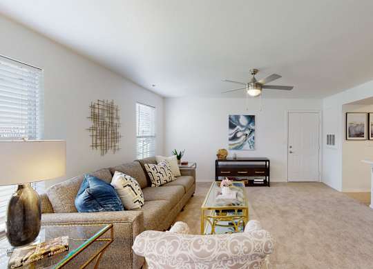 A living room with a couch, coffee table, and a fan.