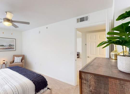 A bedroom with a bed, a ceiling fan, and a painting on the wall.