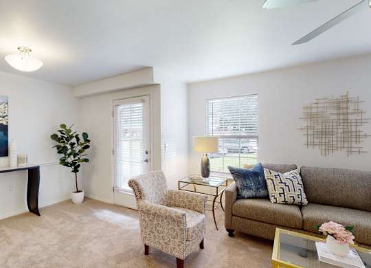 A living room with a grey couch, a yellow bowl on a black table, a painting on the wall, a plant, a chair, and a coffee table.