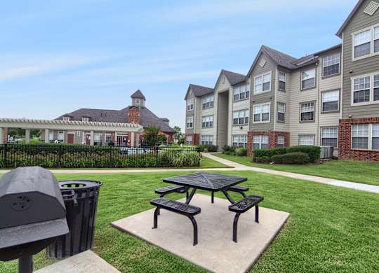 A black picnic table is in the middle of a grassy area in front of apartment buildings.