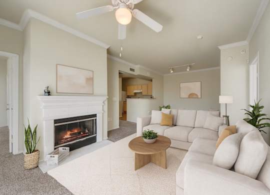 A living room here at Woodland Park with a light beige sofa set, cream rug, and round wood coffee table, centered around a white fireplace, with soft green walls, crown molding, and a white ceiling fan overhead.