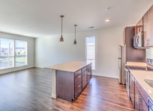 Spacious, modern kitchen with hardwood floors, a large island, pendant lights, and bright natural light at Stitchweld Apartments.