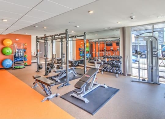Modern gym with weightlifting equipment, exercise balls, and mirrors. Bright and spacious with warm-toned walls, creating an inviting atmosphere at Stitchweld Apartments.