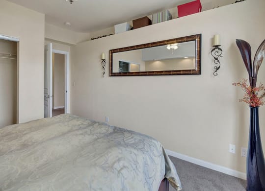 Minimalist bedroom here at Park Plaza 2 Apartments with a bed covered in a patterned comforter, a wall mirror, intricate metal sconces, and a tall vase with dried flowers, creating a serene ambiance.