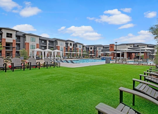 49 West's modern apartment complex with a pool area, surrounded by lush grass and chairs. Bright, sunny day with scattered clouds, creating a serene atmosphere.