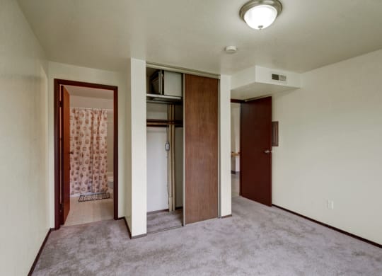 Empty bedroom here at Ptarmigan Meadows with beige carpet and white walls. An open closet with wooden sliding doors is on the right, and a bathroom visible through a door on the left.
