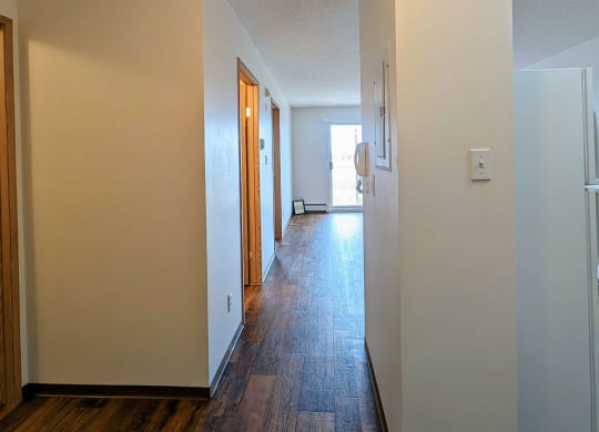 a hallway with white walls and wood flooring and a door to a kitchen