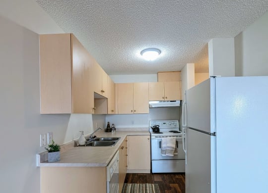an empty kitchen with white appliances and wooden floors