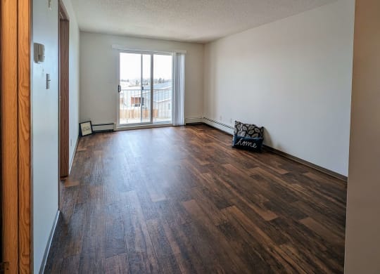 an empty living room with wood flooring and a door to a balcony