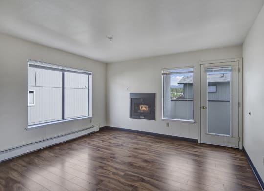 Empty living room here at Silver Ridge Apartments with light wood flooring, white walls, and a modern fireplace. Large windows and a glass door provide natural light. Cozy and minimalistic.