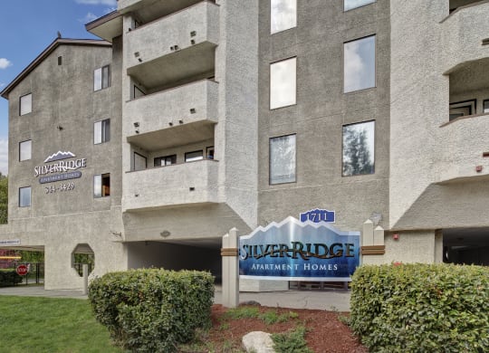 Exterior of Silver Ridge Apartment Homes, featuring textured gray walls, multiple balconies, and a prominent blue sign with the address number 1711.