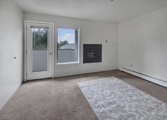 Empty living room here at Silver Ridge Apartments with white walls, a glass door, and a window showing trees outside. A fireplace is set into the wall, and a carpet with floral patterns lies on the floor.