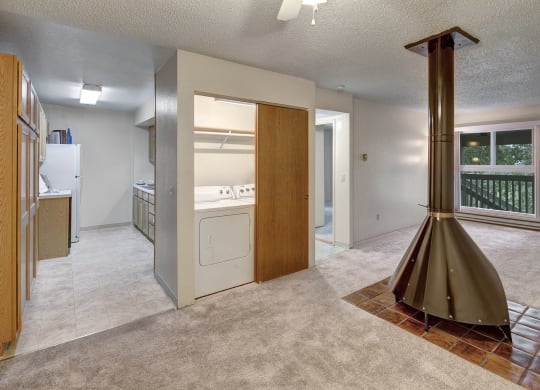 Open-plan living space here at Terrace on the Lake Apartments with beige carpet, a central vintage cone fireplace, and a windowed door leading to a balcony. Adjacent is a utility room with a washer and dryer.