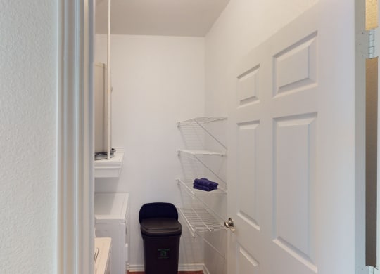 a small closet in a bathroom with a trash can and a white door