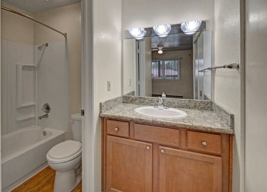Compact bathroom here at The Club at Eagle Pointe Apartments with wooden vanity, granite countertop, and a white sink. A large mirror reflects a bright room with a window and ceiling fan.