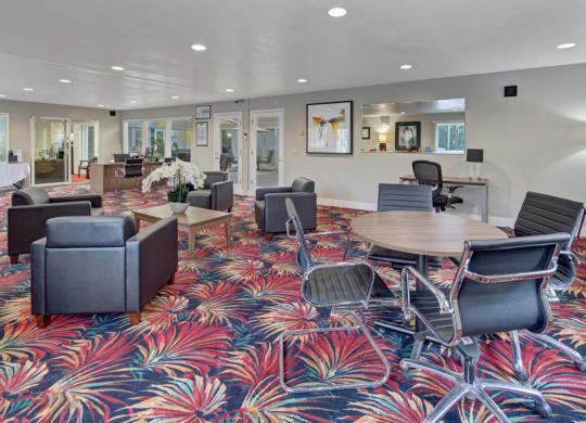 Modern office lobby here at The Club at Eagle Pointe Apartments with vibrant red and blue floral carpet, featuring gray armchairs, wood tables with orchids, and sleek black office chairs. Bright and welcoming atmosphere.