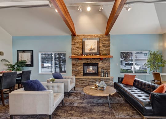 A cozy resident lounge here at The Highlands Luxury Apartments with a stone fireplace, wooden beams, and modern furniture. Soft lighting and pillows create a warm, inviting atmosphere.