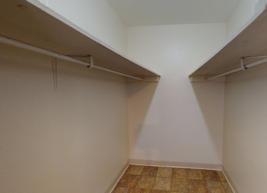 Empty walk-in closet here at the Village at Calais Apartments with beige walls, two white shelves on opposite sides, and tiled floor. The space appears clean, spacious, and well-lit.