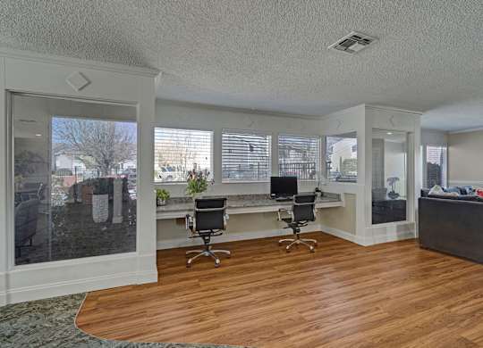 A room with a desk and chairs in front of a window.