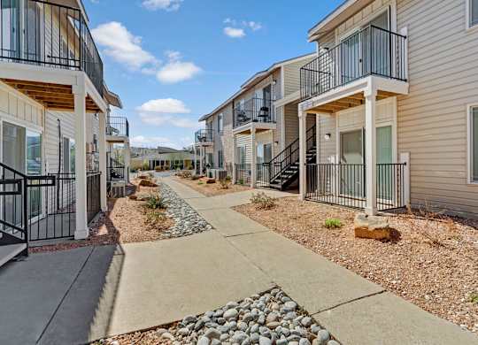 A sunny exterior walkway at Acacia Park featuring private balconies and patios, clean concrete paths, low-maintenance landscaping, and a welcoming layout that makes moving around the community easy and comfortable.