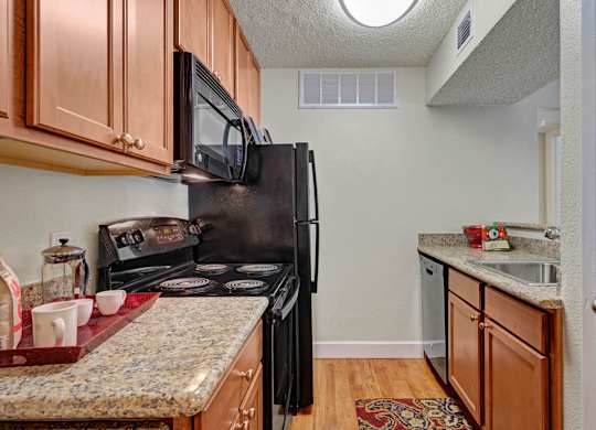 A bright kitchen at Acacia Park with warm wood cabinetry, granite-style countertops, modern black appliances, and efficient overhead lighting that creates a practical and inviting cooking space.