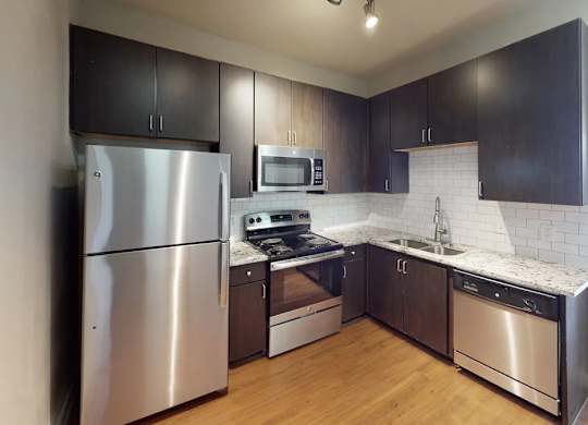 A modern kitchen here at BRIO at Firewheel with dark wood cabinets, granite countertops, white tile backsplash, stainless steel appliances, and wood-style flooring in a clean, updated layout.