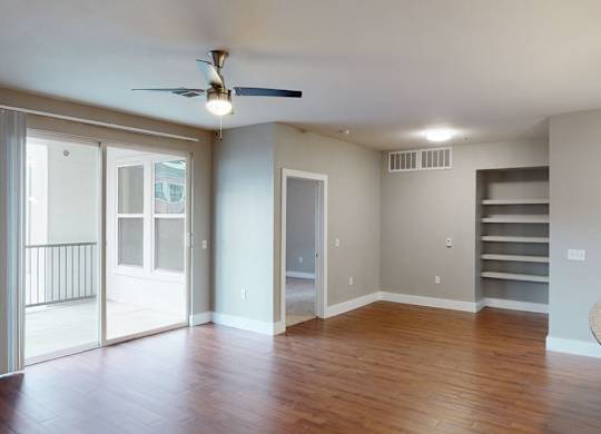 A spacious open living area here at BRIO at Firewheel with wood-style flooring, ceiling fan, sliding glass doors to a balcony, built-in shelving, and an open layout connected to the kitchen.