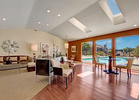 A spacious resident lounge here at Cypress Pointe with modern décor, comfortable seating, and warm wood-style flooring creating a welcoming atmosphere. An open layout with decorative accents, soft lighting, and views into adjacent gathering areas offers an inviting space for relaxing or socializing.